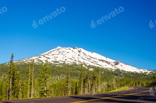 Preview: A Highway Leading Through A Forest Passing Next To Snowy Mount Bachelor Near Bend, Oregon