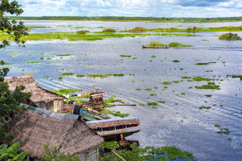 Preview: Shacks On The Riverfront Of Iquitos, Peru With A Canoe Passing By In The Background