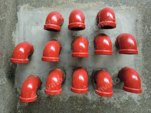 Preview: Many Vibrant Red Pipe Elbows Arranged In Pattern On Concrete Wall