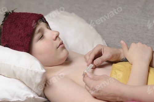 Preview: Sick Child With High Fever Laying In Bed And Holding Thermometer