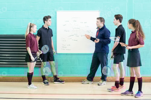 Visualização: Foto completa de um professor de ginástica ensinando badminton para estudantes do ensino médio no ginásio.