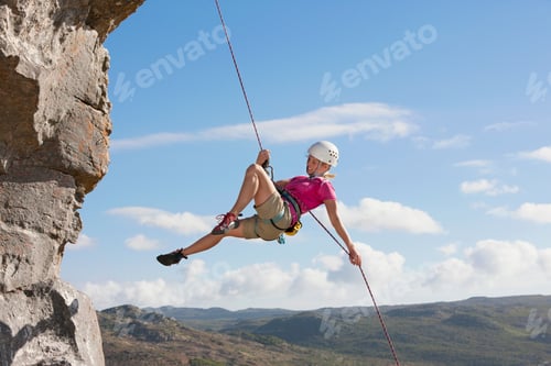 Preview: Wide Shot Of The Side View Of A Female Rock Climber Abseiling Down A Rock Face.