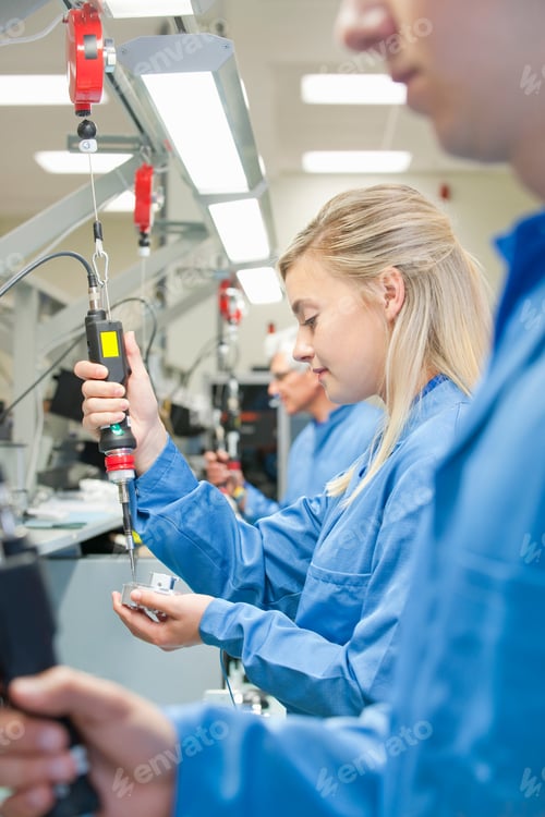 Preview: Vertical Shot Of Young Technicians In Aprons Using Electric Screwdrivers To Assemble Machine Parts