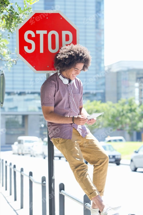 Preview: Young Man Standing On A Railing Leaning Against A Stop Sign And Using A Digital Tablet