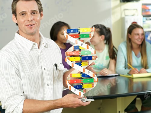 Preview: Teenagers Sitting At Desks With Focus On Male Teacher Holding Dna Model In Foreground In A