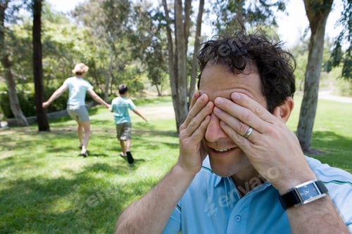 Vista previa: Family Playing Hide And Seek In Park With Boy And Mother Running As The Man Covers Eyes In