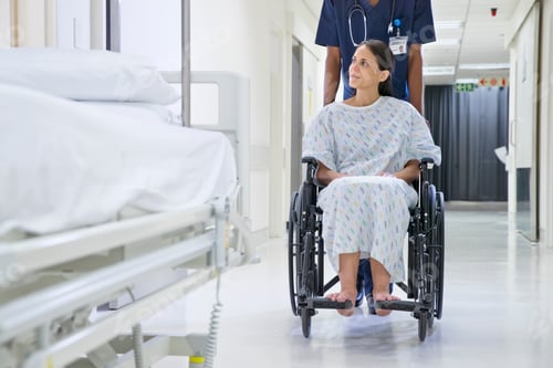 Preview: Male Nurse Pushing Patient Along Hospital Corridor In Wheelchair