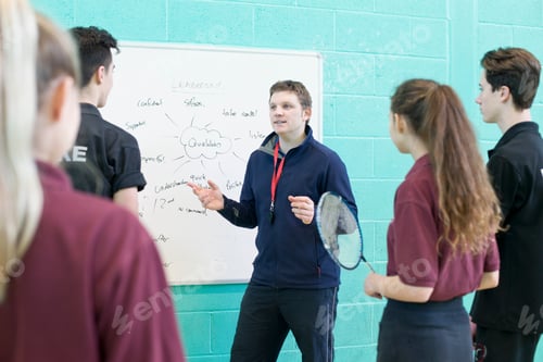 Visualização: Foto média de um professor de ginástica ensinando badminton para estudantes do ensino médio no ginásio.