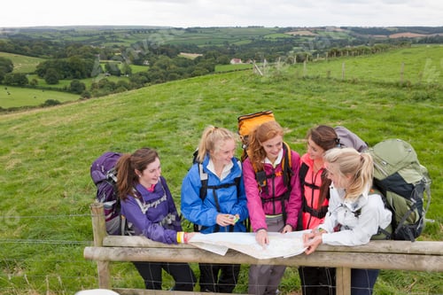 Preview: High-Angle Shot Of A Group Of Girls With Backpacks Looking At A Map And Compass Over A Wooden Fence