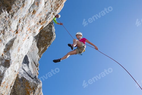 Preview: Low-Angle Shot Of A Female Rock Climber Abseiling Down A Rock Face With A Man Watching Her.