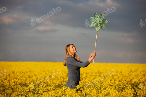 Preview: A Young Woman Standing In A Rape Seed Field Holding A Windmill