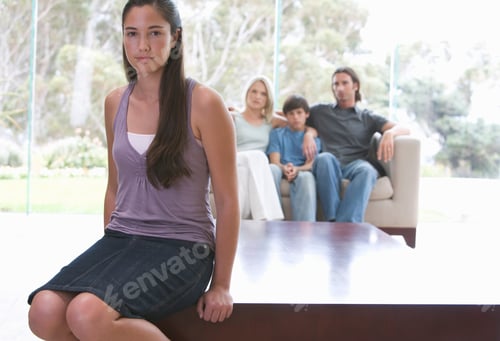 Preview: A Young Girl Sitting On A Coffee Table With Her Family On The Sofa