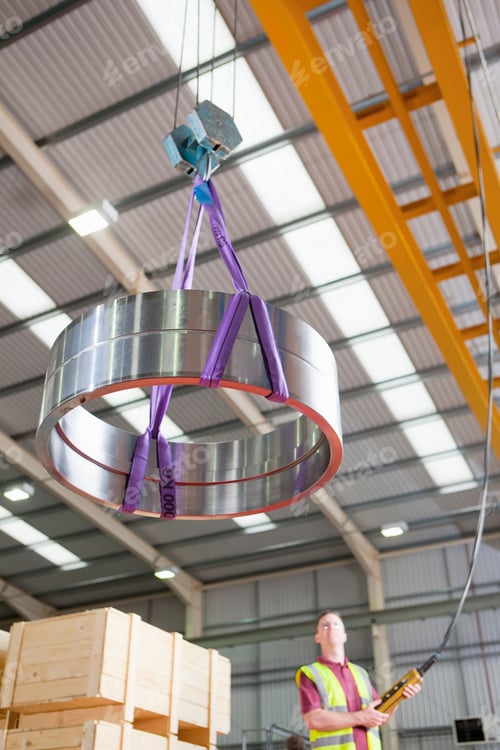 Preview: Low-Angle Wide Shot Of A Steel Roller Bearing Being Moved By A Worker Using A Hoist At A