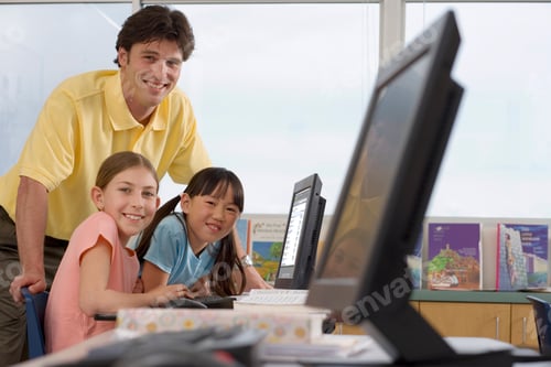 Preview: Teacher Helping Female Elementary Students Working On Computers At Desk In It Class At Camera