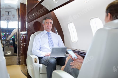 Preview: Smiling Businessman Sitting In A Private Jet And Working On A Digital Tablet While Talking To A