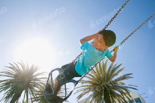Preview: Boy Swinging Near Palm Trees At A Playground