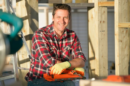 Portrait Of Carpenter Holding Nailgun On Indoor Building Construction Site And Smiling At Camera