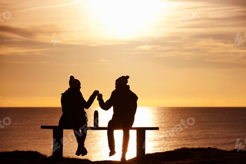Preview: Silhouette Of A Couple Sitting On A Bench And Enjoying Drinks Against The Sunset Over The Ocean.