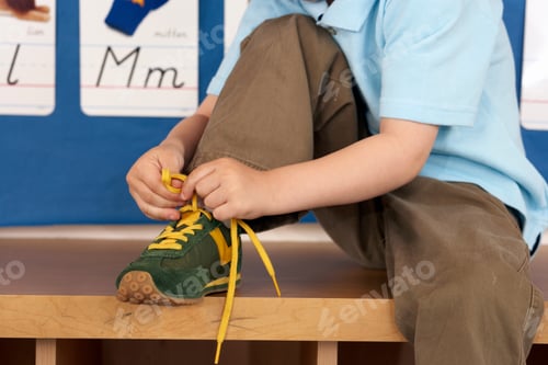 Preview: Close Up Shot Of A Boy Tying His Shoe Lace While Sitting On A Wooden Storage Cabinet In His