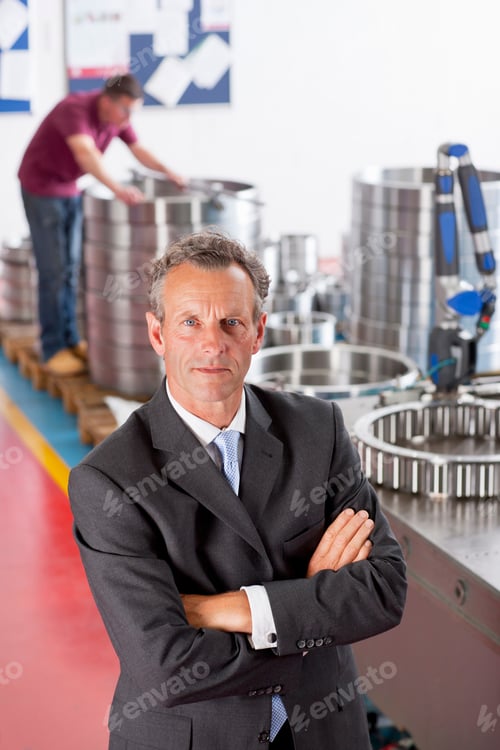 Preview: Vertical Portrait Of A Male Manager In A Suit Looking At The Camera With A Worker In The Background