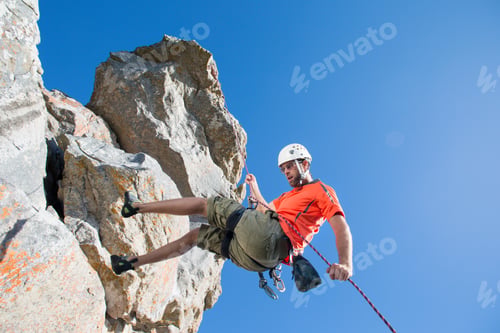 Preview: Male Rock Climber In A Helmet Holding On To A Rope While Rappelling Down A Rock Face.