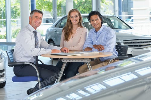 Preview: Portrait Of Smiling Salesman And Couple At A Table In A Car Dealership Showroom
