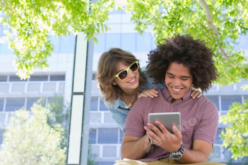Preview: Smiling Young Couple Watching Something Funny On A Digital Tablet In An Urban Park