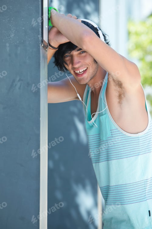 Preview: Vertical Portrait Of A Smiling Young Man Wearing Headphones Leaning Against A Grey Wall