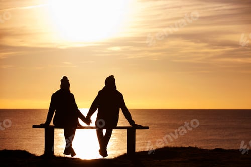 Preview: Silhouette Of A Couple Holding Hands And Sitting On A Bench Against The Sunset Over The Ocean.
