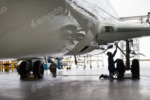 Preview: Wide Shot Of An Engineer Inspecting The Undercarriage Of A Passenger Jet At A Hangar.