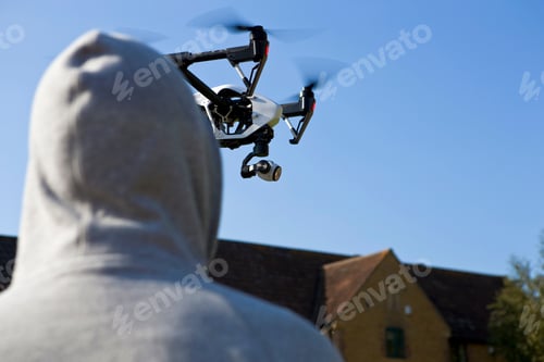 Preview: Hooded Man Looking Up At A Surveillance Drone In The Blue Sky