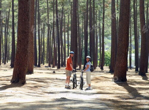 Preview: Rear Profile View Of A Senior Couple In Cycling Helmets Walking Side By Side Through Wood With