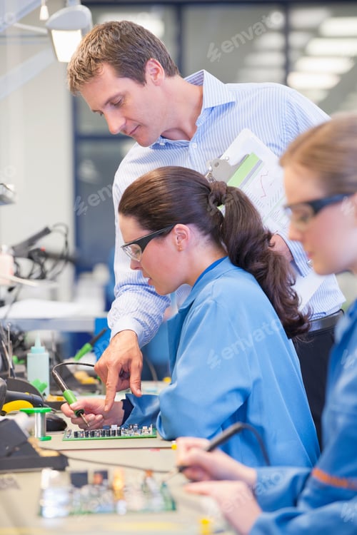 Preview: Vertical Shot Of A Supervisor Training A Fellow Technician To Solder Circuit Board On Production