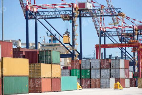 Preview: A Commercial Harbor With Cranes And Cargo Containers Stacked Next To A Ship.