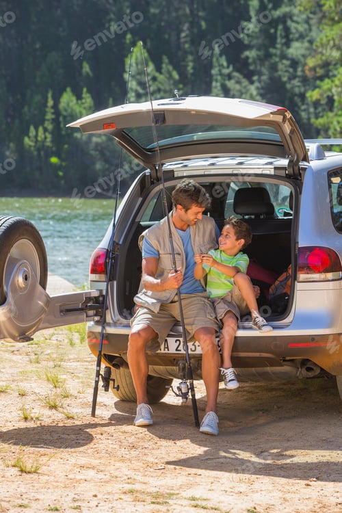 Preview: Vertical Shot Of Father And Son With A Fishing Rod At The Back Of A Car Beside A Lake.
