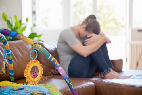 Preview: Unhappy Mother Suffering With Post Natal Depression Sits On Sofa