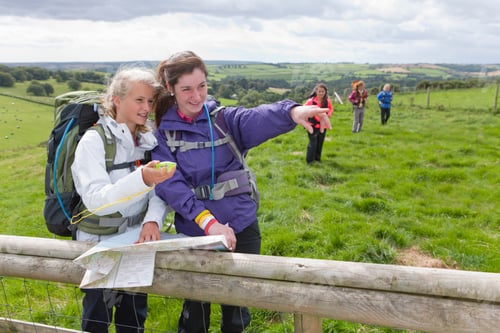 Preview: Girls With A Backpack, Map And Compass Pointing In A Direction With A Group Of Friends In The