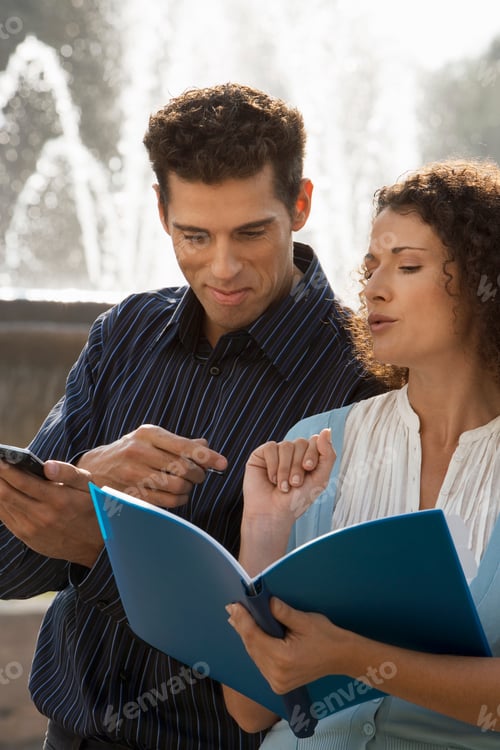 Preview: Vertical Shot Of A Businessman And Businesswoman Looking At Documents In File Near A Fountain