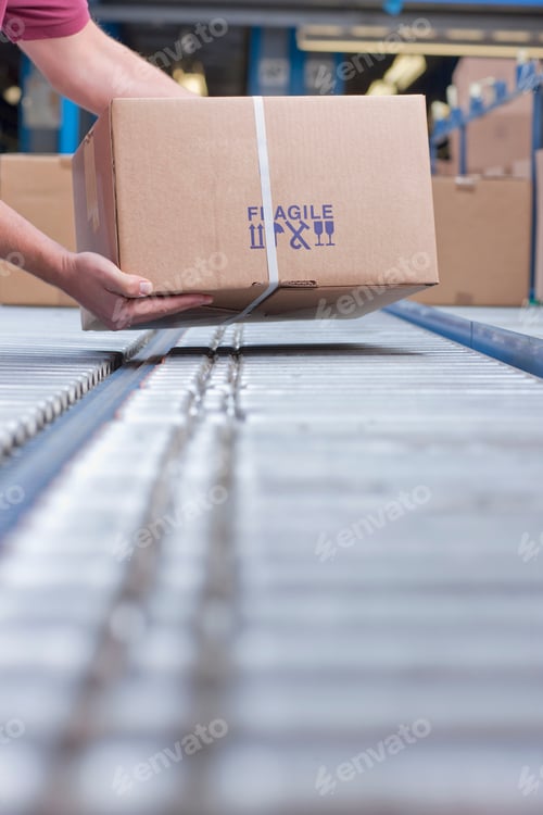 Preview: Close-Up Vertical Shot Of The Hands Of A Worker Placing A Box On Conveyor Belt At A Distribution