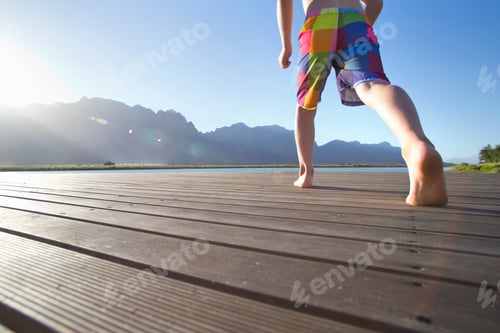 Preview: Low-Angle Shot Of A Boy Running Over A Wooden Jetty To Jump Into The Lake.
