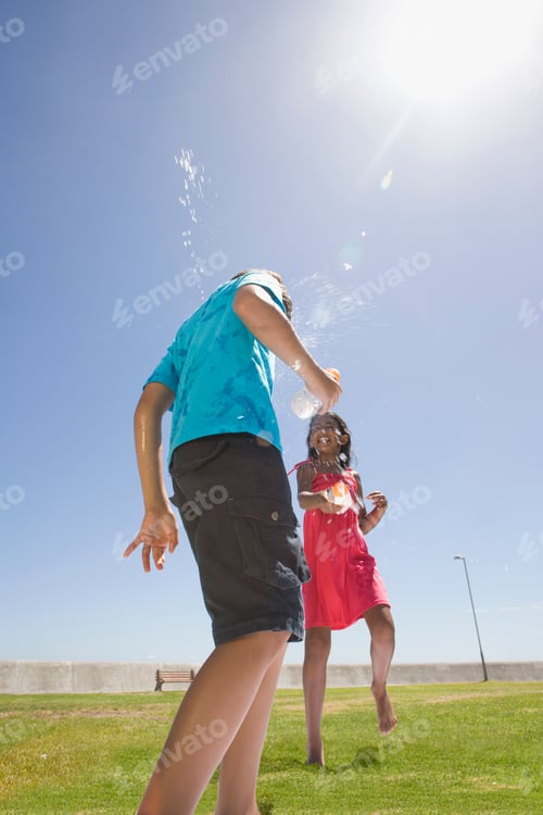 Preview: Vertical Shot Of A Girl Squirting Water At Her Friend At A Park