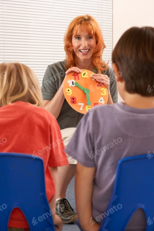 Preview: Vertical Shot Of Children Learning To Tell The Time With Focus On Teacher Holding Colorful Clock In