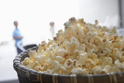 Preview: A Close-Up Shot Of A Bowl Of Popcorn With People In The Background.