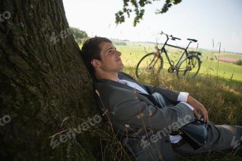 Preview: Young Businessman Leaning On Tree Near Bicycle
