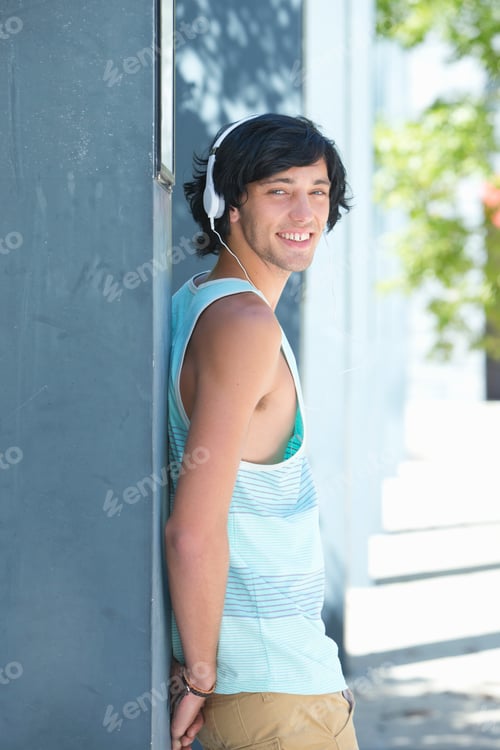 Preview: Vertical Portrait Of A Smiling Young Man Wearing Headphones Leaning Against A Grey Wall
