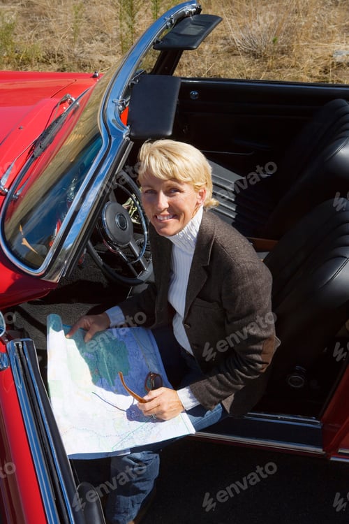 Preview: Mature Woman With Classic Red Convertible Car On Road Trip Using Map
