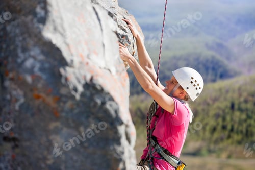 Preview: Side View Of A Tired Female Rock Climber Scaling Up A Rock Face.