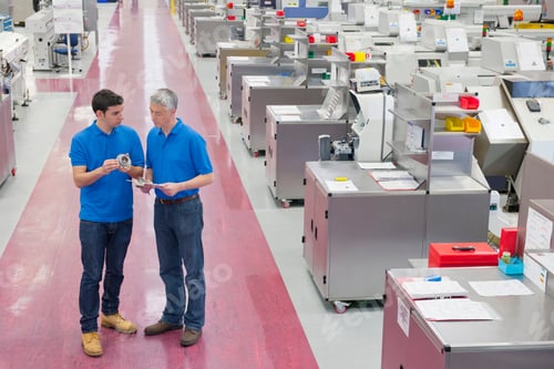 Preview: Medium Wide Shot Of Two Engineers Standing In The Aisle Of A Manufacturing Plant While Examining A