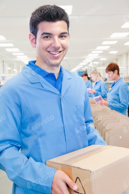 Preview: Portrait Shot Of A Male Worker In Apron Smiling At The Camera While Holding A Cardboard Box In A