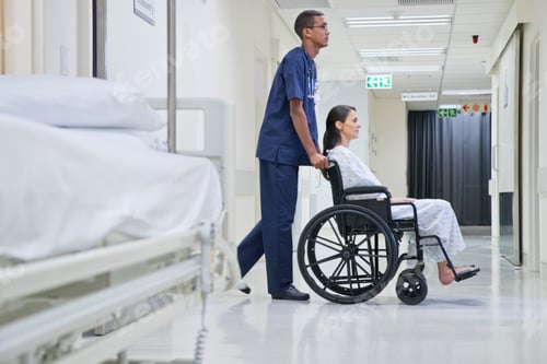 Preview: Male Nurse Pushing Patient Along Hospital Corridor In Wheelchair
